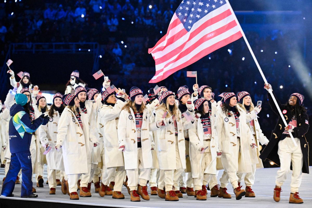 Team USA athletes at the 2026 Milan Cortina Olympics Opening Ceremony. They are seen waving little USA flags in their Opening Ceremony uniforms. 