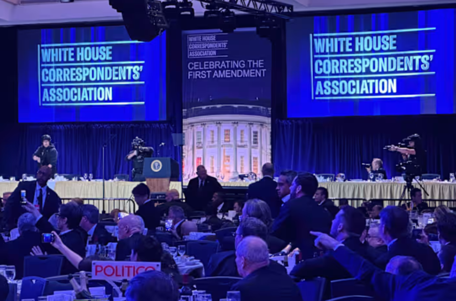 The photo shows the aftermath of the shooting incident at the White House Correspondents’ Dinner. Attendees are ducked down and taking videos with their phones and law enforcement is surveying the scene. 